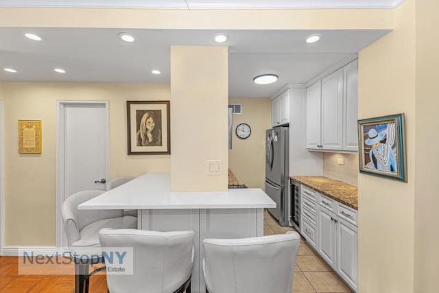 kitchen featuring tasteful backsplash, freestanding refrigerator, recessed lighting, a peninsula, and a breakfast bar area