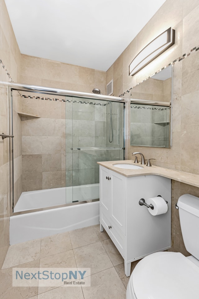 bathroom with tile walls, toilet, bath / shower combo with glass door, and tile patterned floors