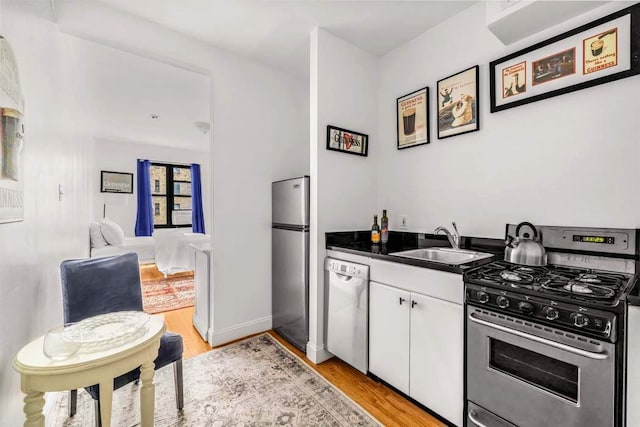 kitchen featuring light wood-style flooring, a sink, dark countertops, stainless steel appliances, and white cabinets