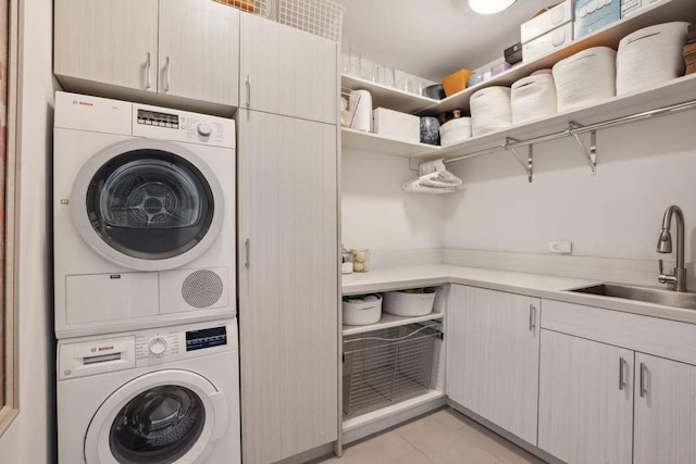 washroom with light tile patterned floors, cabinet space, stacked washing maching and dryer, and a sink