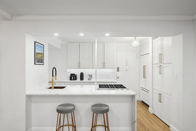 kitchen with a sink, a kitchen breakfast bar, white cabinets, and ornamental molding