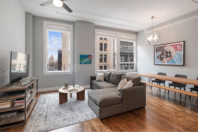 living area featuring ceiling fan with notable chandelier, baseboards, and wood finished floors