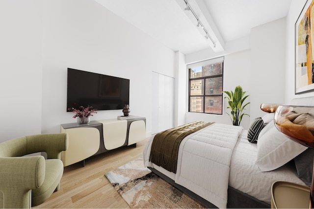 bedroom with beamed ceiling, rail lighting, wood finished floors, and a closet