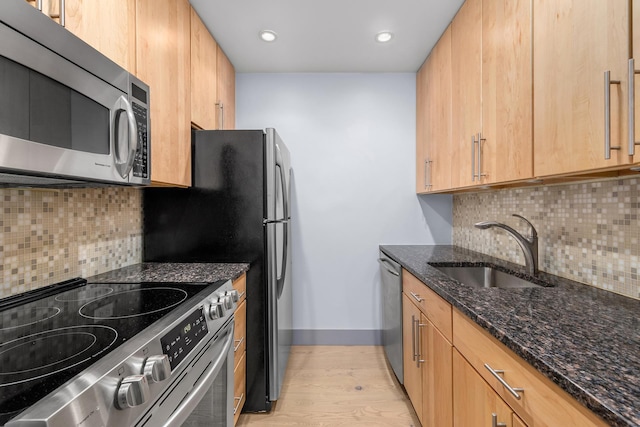 kitchen featuring baseboards, dark stone counters, a sink, stainless steel appliances, and light wood-style floors