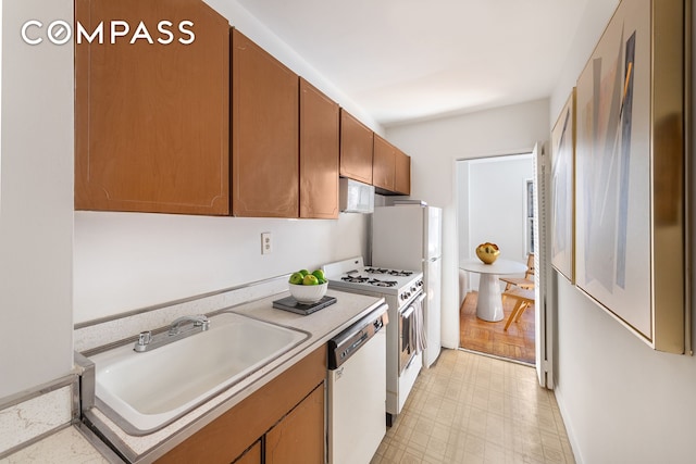 kitchen featuring white appliances, brown cabinetry, light floors, a sink, and light countertops