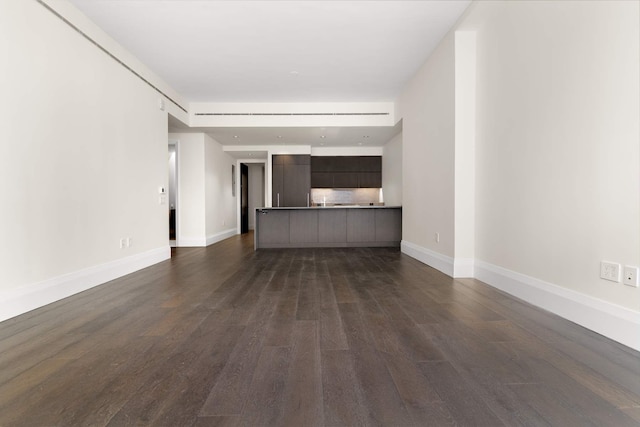 unfurnished living room featuring baseboards and dark wood-style flooring