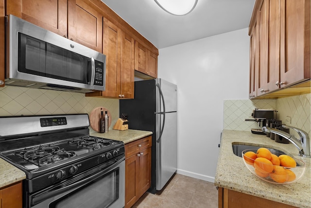 kitchen featuring a sink, tasteful backsplash, appliances with stainless steel finishes, light tile patterned flooring, and light stone countertops