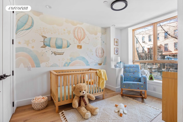 bedroom featuring baseboards, a crib, and wood finished floors