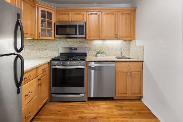 250 W 88th St Unit 503, New York City, NY 10024 - kitchen with appliances with stainless steel finishes, light wood-type flooring, glass insert cabinets, light stone counters, and decorative backsplash