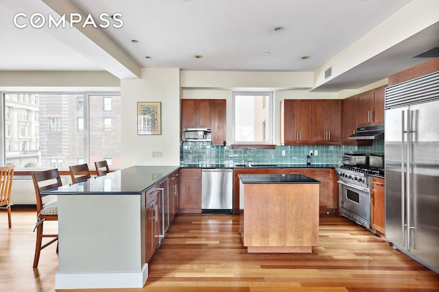 kitchen with visible vents, under cabinet range hood, a kitchen bar, a peninsula, and high end appliances