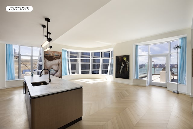 kitchen with visible vents, a center island with sink, a sink, baseboards, and hanging light fixtures