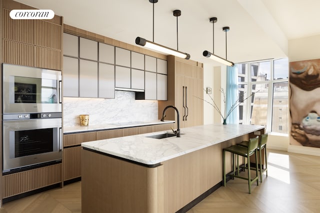 kitchen with a sink, light stone counters, cooktop, a breakfast bar area, and decorative backsplash