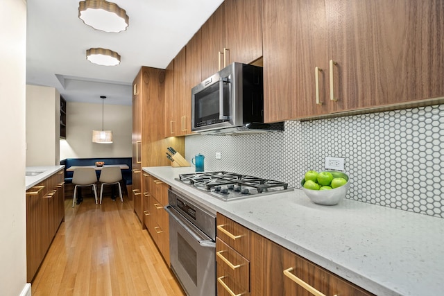 kitchen featuring light wood-style floors, brown cabinetry, tasteful backsplash, and appliances with stainless steel finishes