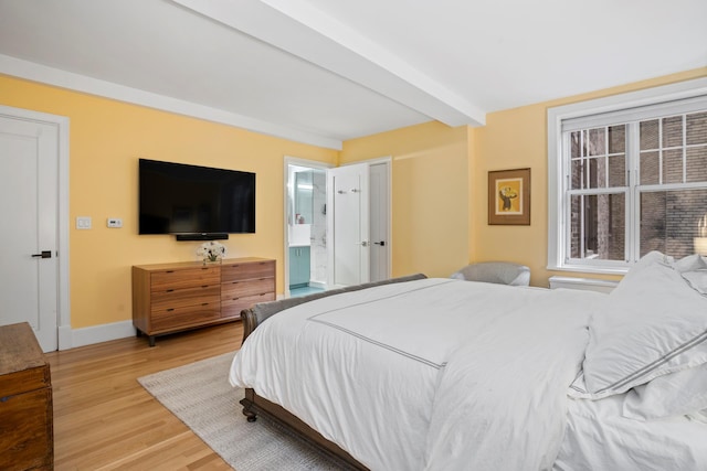 bedroom featuring beamed ceiling, baseboards, ensuite bath, and wood finished floors