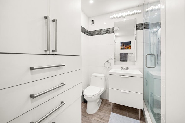 bathroom with toilet, a stall shower, wood finished floors, tile walls, and vanity