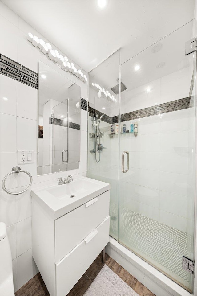 full bath with vanity, a shower stall, wood finished floors, and tile walls