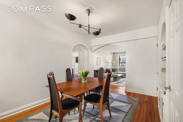 dining space with baseboards, arched walkways, and wood finished floors