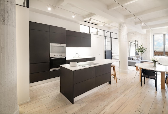 kitchen with modern cabinets, light wood-style flooring, a sink, a kitchen island, and dark cabinetry