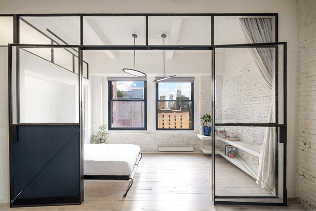 bedroom with brick wall, baseboard heating, and hardwood / wood-style floors