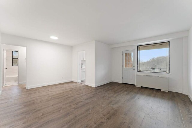 empty room with radiator heating unit, wood finished floors, and baseboards