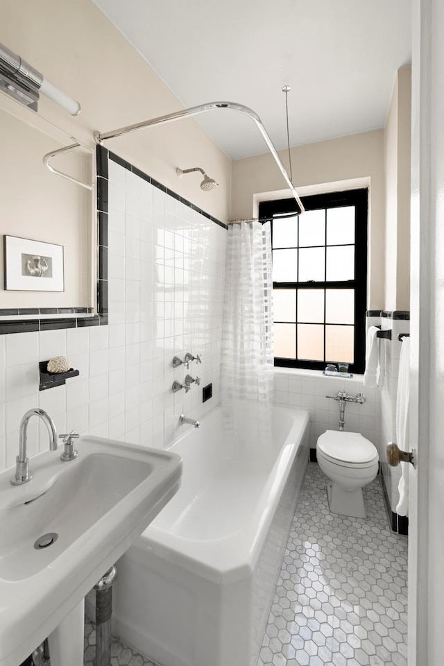 full bath featuring toilet, tile patterned floors, shower / bath combination with curtain, tile walls, and a sink