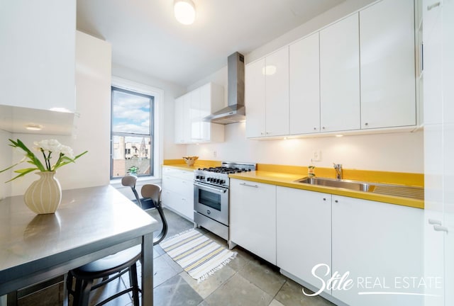 kitchen featuring a sink, light countertops, white cabinets, high end stainless steel range, and wall chimney range hood