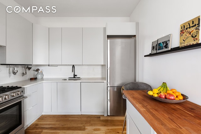 kitchen with tasteful backsplash, butcher block countertops, light wood-type flooring, appliances with stainless steel finishes, and a sink