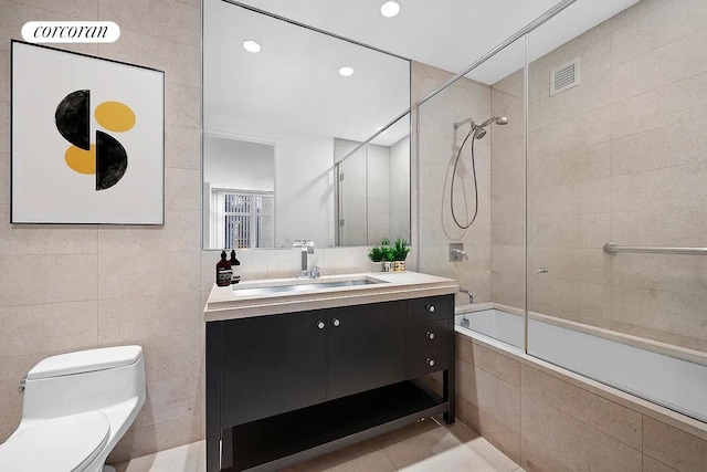 bathroom featuring visible vents, toilet, tiled shower / bath combo, tile walls, and vanity