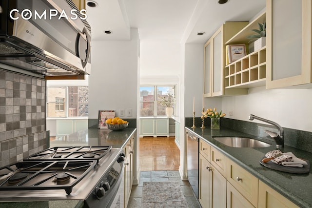 kitchen with dark stone countertops, a sink, cream cabinetry, appliances with stainless steel finishes, and tasteful backsplash