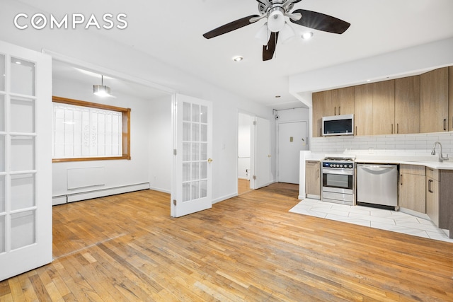 kitchen featuring a baseboard heating unit, light countertops, decorative backsplash, appliances with stainless steel finishes, and a sink