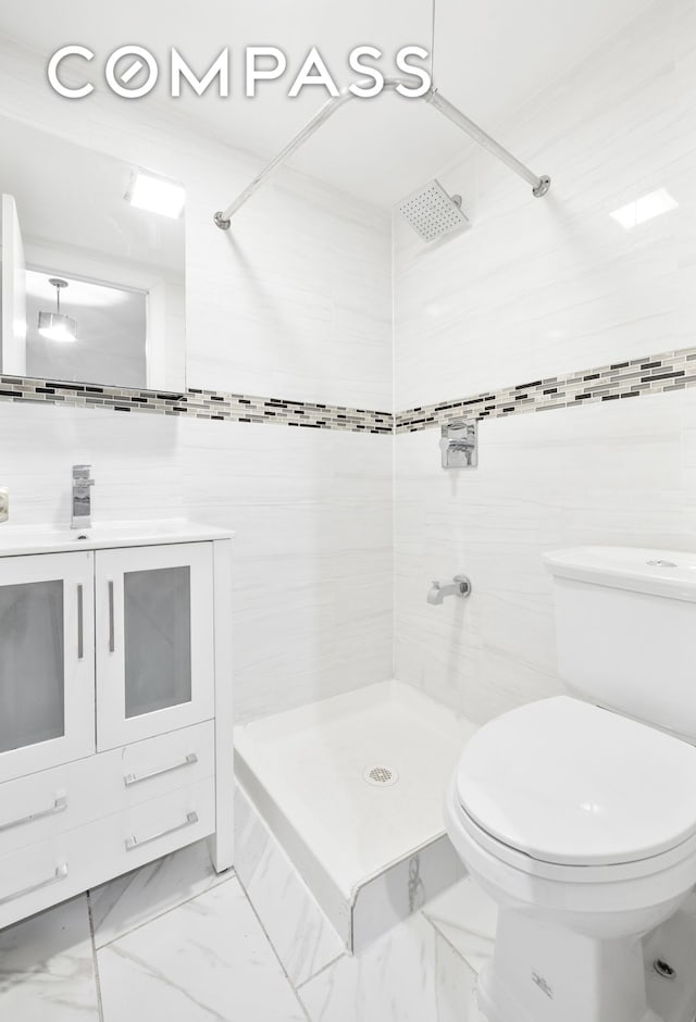 bathroom with vanity, a tile shower, tile walls, toilet, and marble finish floor