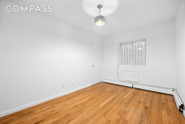 spare room featuring baseboards, a baseboard heating unit, and light wood-style floors