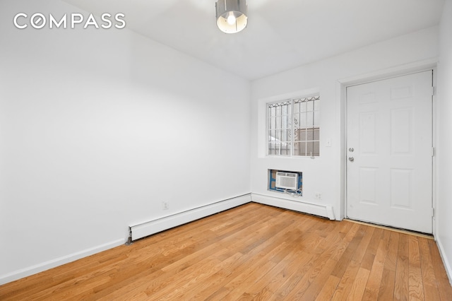 spare room with a baseboard heating unit, light wood-style floors, baseboards, and a wall mounted AC