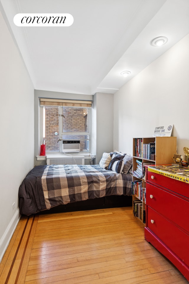 bedroom with cooling unit, baseboards, and wood-type flooring