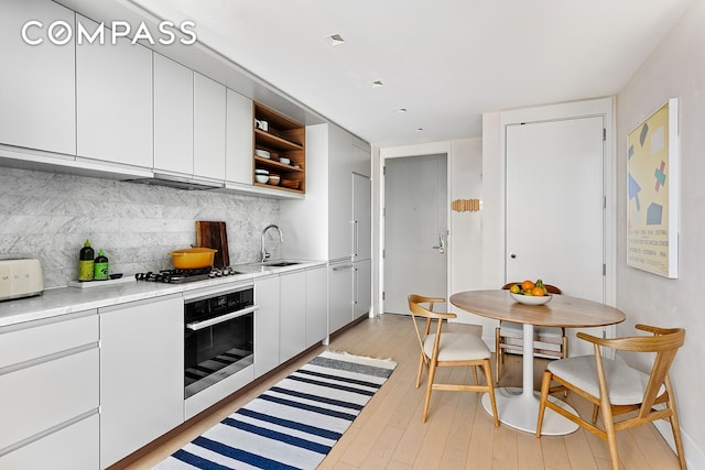 kitchen featuring light wood finished floors, open shelves, oven, decorative backsplash, and light countertops