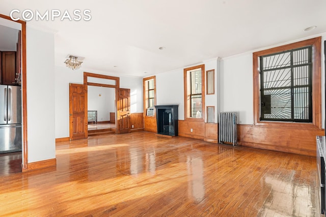 unfurnished living room with crown molding, radiator, light wood-style floors, and a wainscoted wall