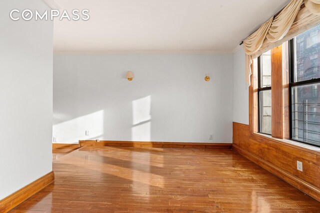 empty room with baseboards, ornamental molding, wood walls, and hardwood / wood-style flooring