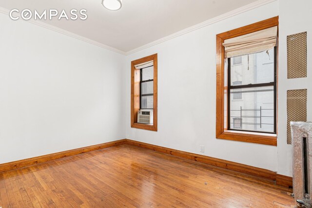 empty room featuring radiator, wood-type flooring, baseboards, and ornamental molding