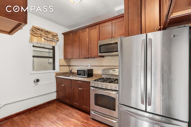 kitchen with baseboards, decorative backsplash, wood finished floors, stainless steel appliances, and a sink