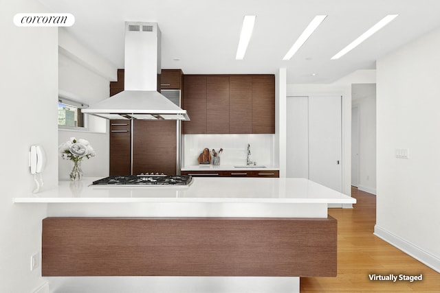 kitchen with a peninsula, a sink, stainless steel gas stovetop, modern cabinets, and island range hood