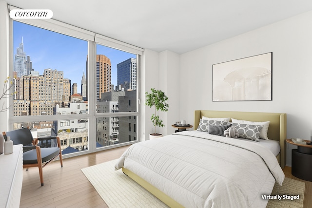 bedroom featuring visible vents, a view of city, a wall of windows, and wood finished floors