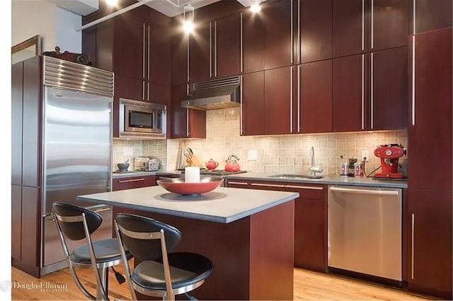 kitchen featuring under cabinet range hood, built in appliances, decorative backsplash, a kitchen breakfast bar, and a sink