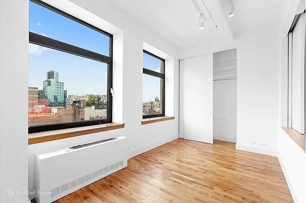 empty room featuring wood finished floors, baseboards, radiator heating unit, track lighting, and a city view