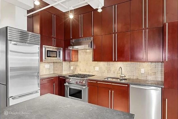 kitchen with a sink, decorative backsplash, built in appliances, and under cabinet range hood