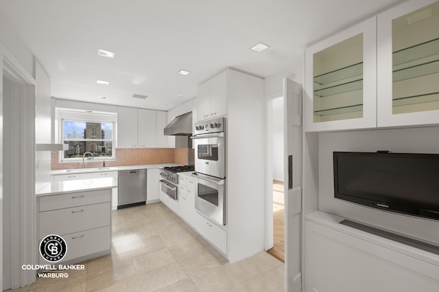 kitchen featuring light countertops, stainless steel appliances, white cabinetry, wall chimney exhaust hood, and a sink