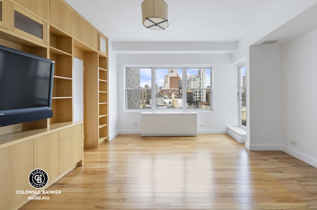 unfurnished living room with a city view, baseboards, and light wood-style floors