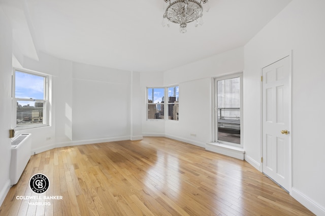 unfurnished room featuring radiator, light wood-style floors, baseboards, and a chandelier