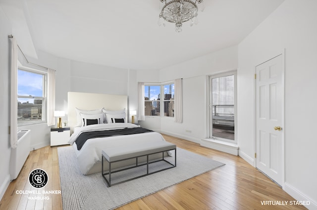 bedroom with a notable chandelier, baseboards, and light wood-type flooring