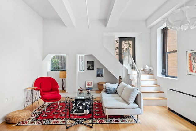 living area with beam ceiling, stairway, radiator heating unit, and wood finished floors