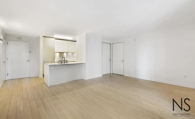 kitchen featuring white cabinetry, light wood-type flooring, light countertops, and a peninsula